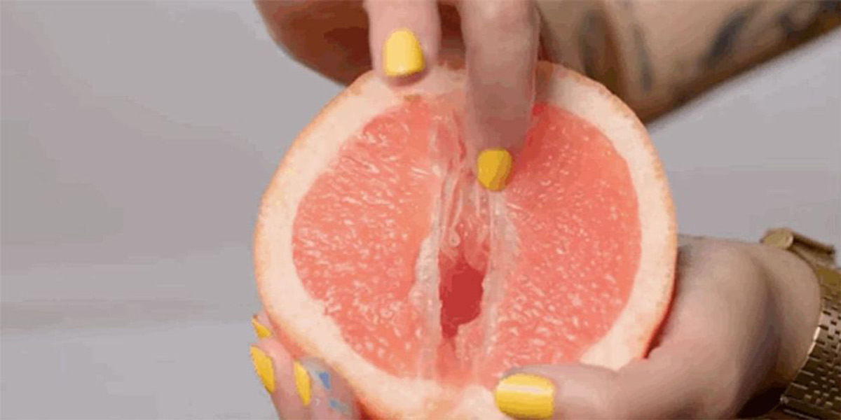 Finger with yellow nail polish stroking the core of a grapefruit imitating female genital stimulation